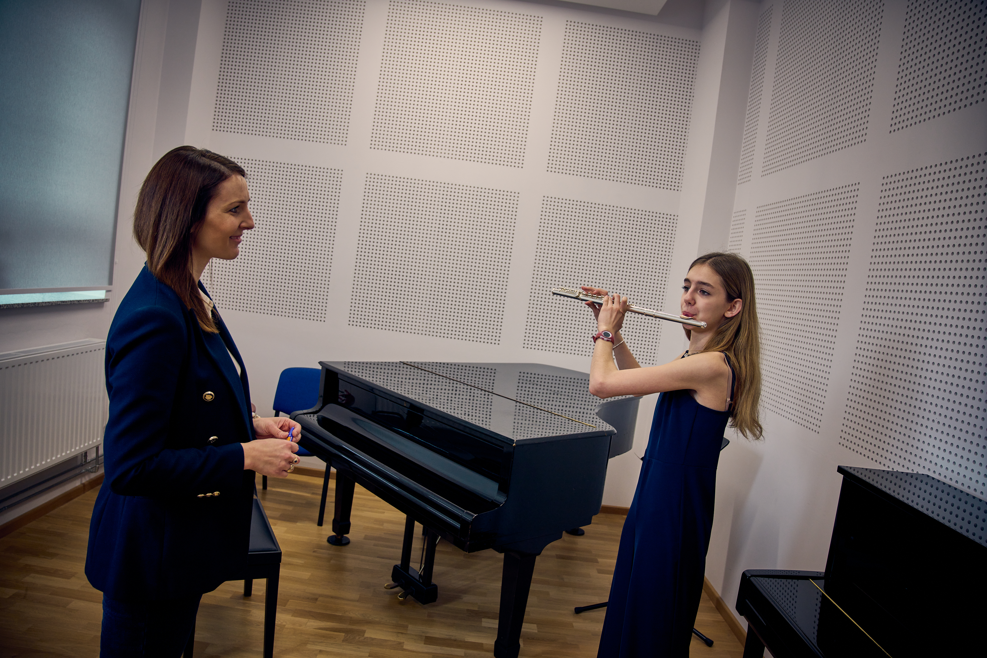 Dziewczynka gra na flecie, naprzeciwko stoi nauczycielka