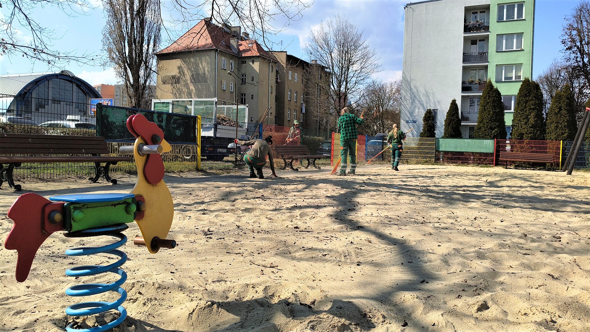 trzy panie spsrzątaja plac zabaw. Na pierwszym planie kiwaczek w kształcie konika