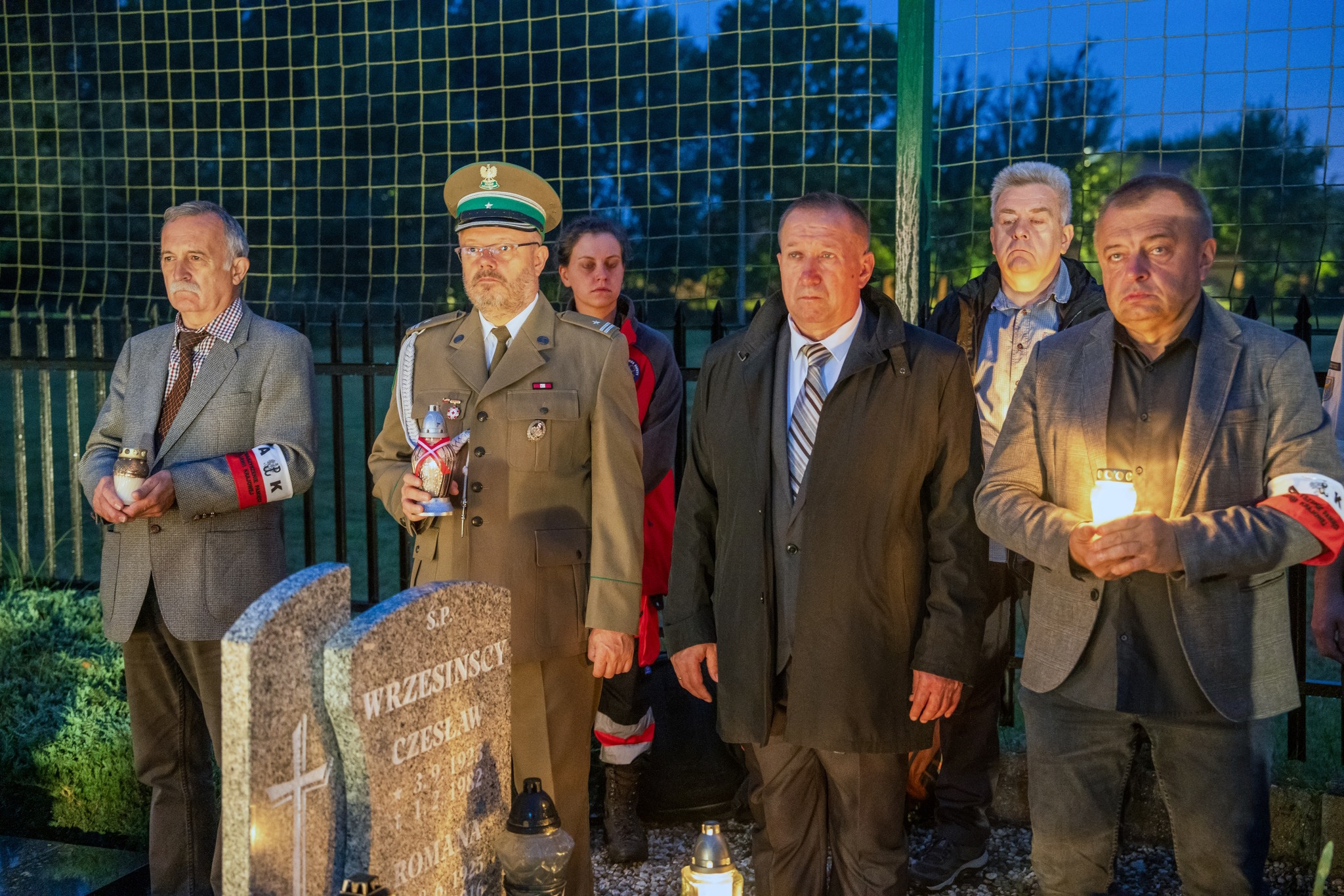 Uczestnicy obchodów stoją ze zniczami na cmentarzu