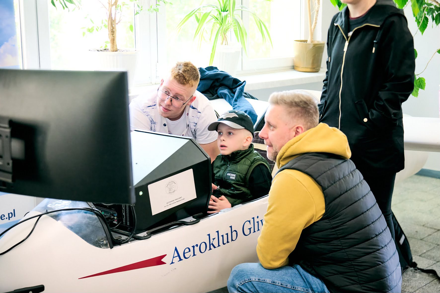 dziecko w szybowcu, dorosły kuca obok