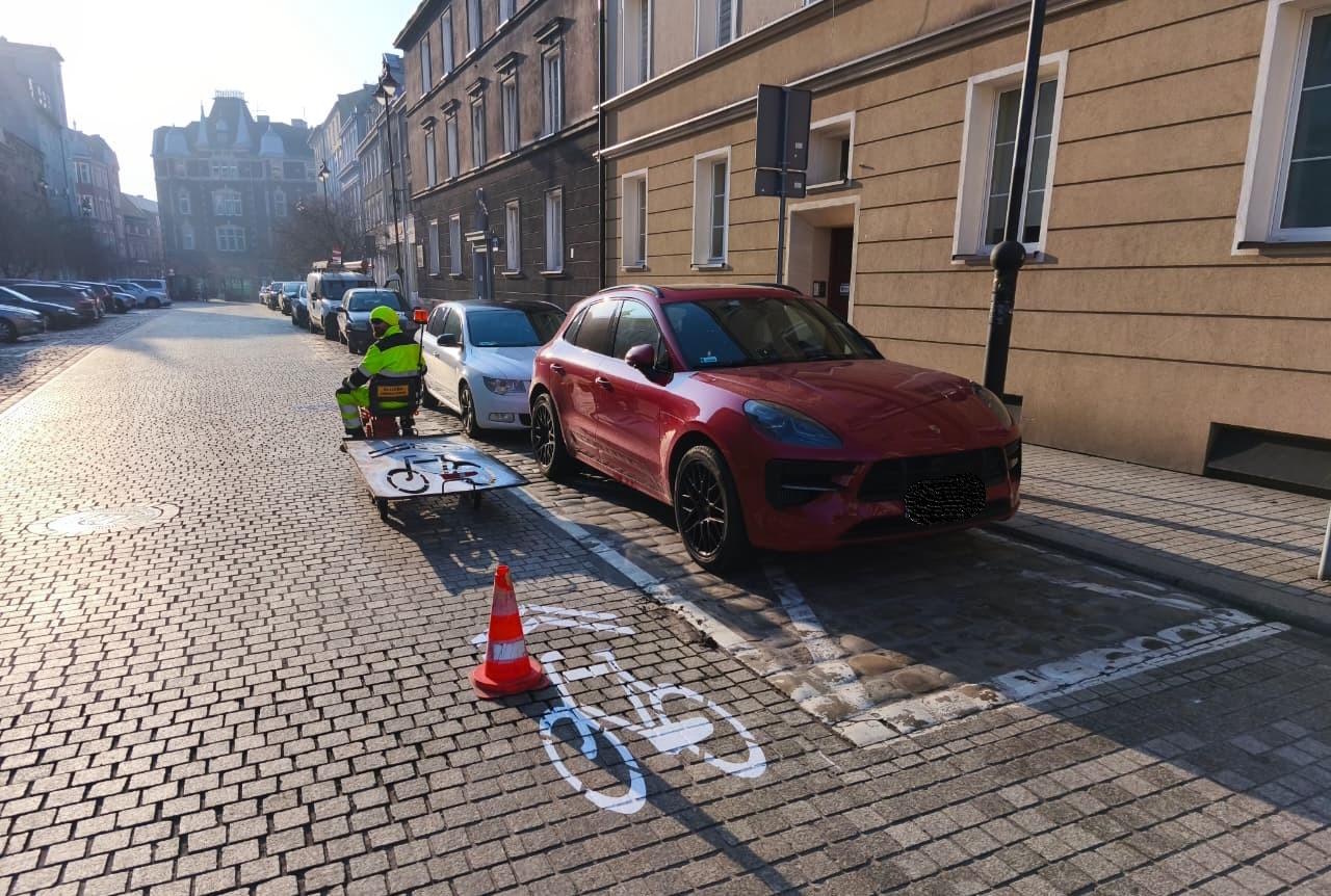 starówka i człowiek przy samochodzie. Na jezdni namalowany znak poziomy w kształcie roweru