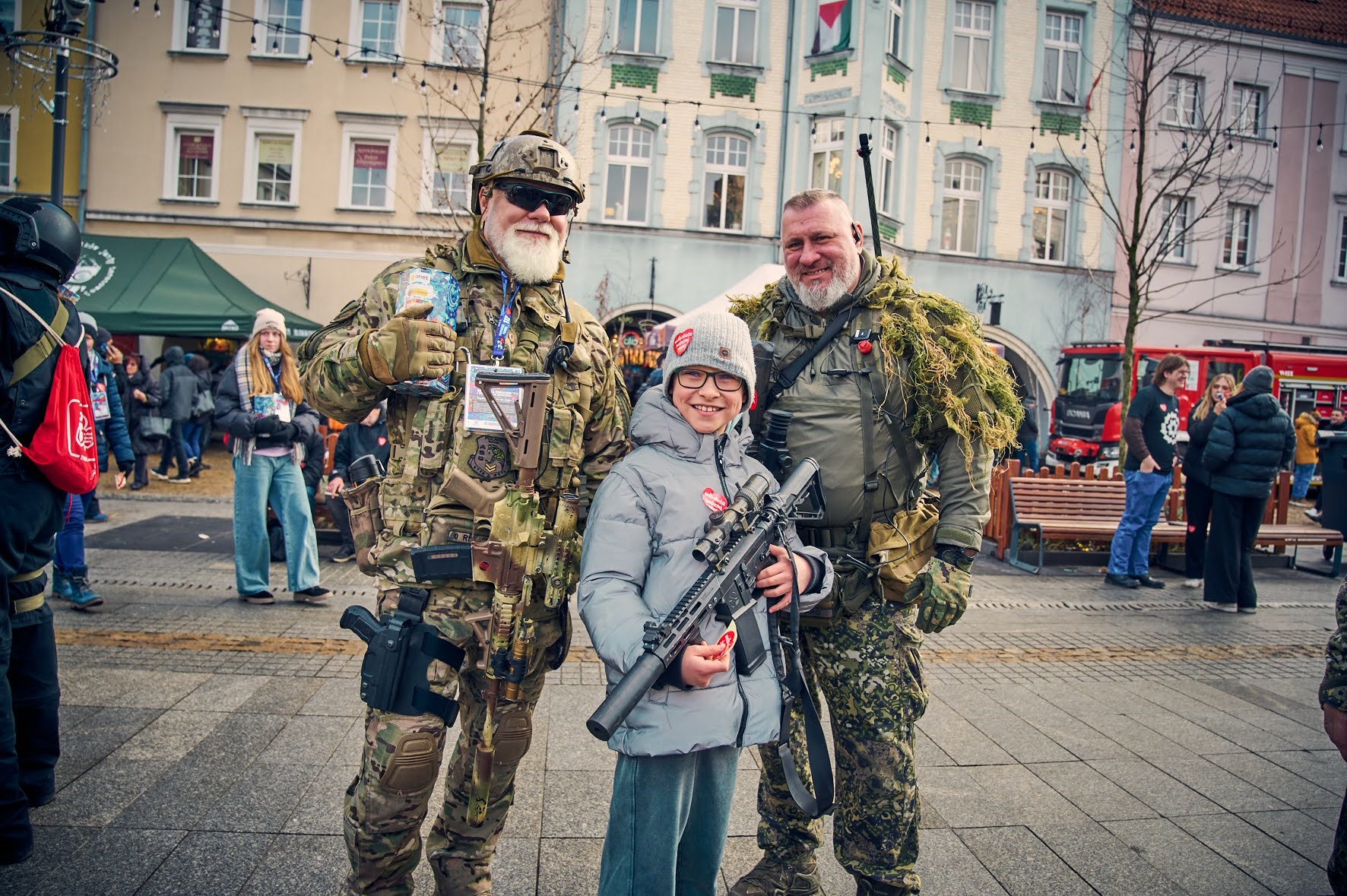 Mężczyźni w strojach wojskowych i chłopiec z karabinem pozują do zdjęcia