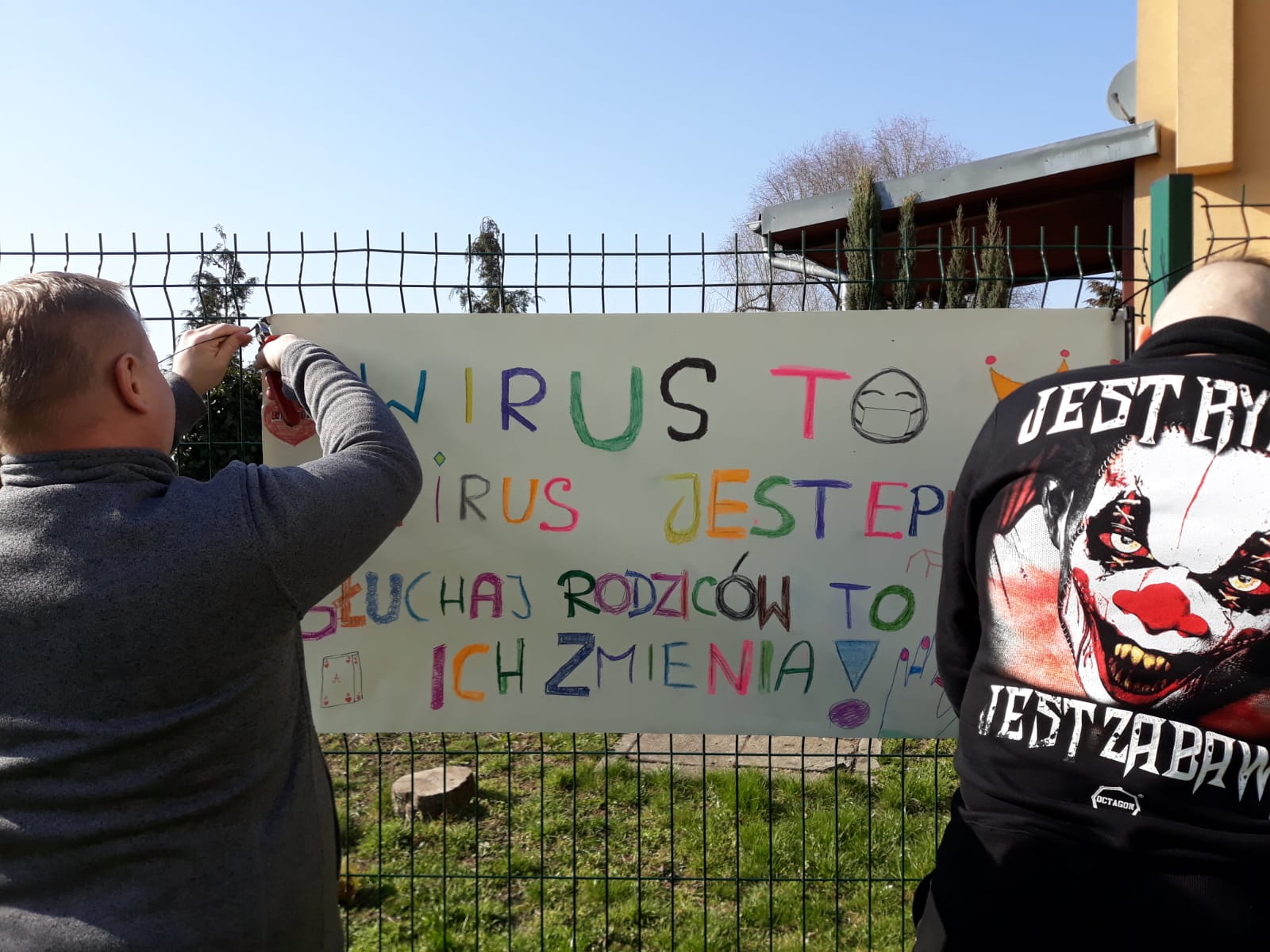 wychowawca i młody chłopak wieszają baner