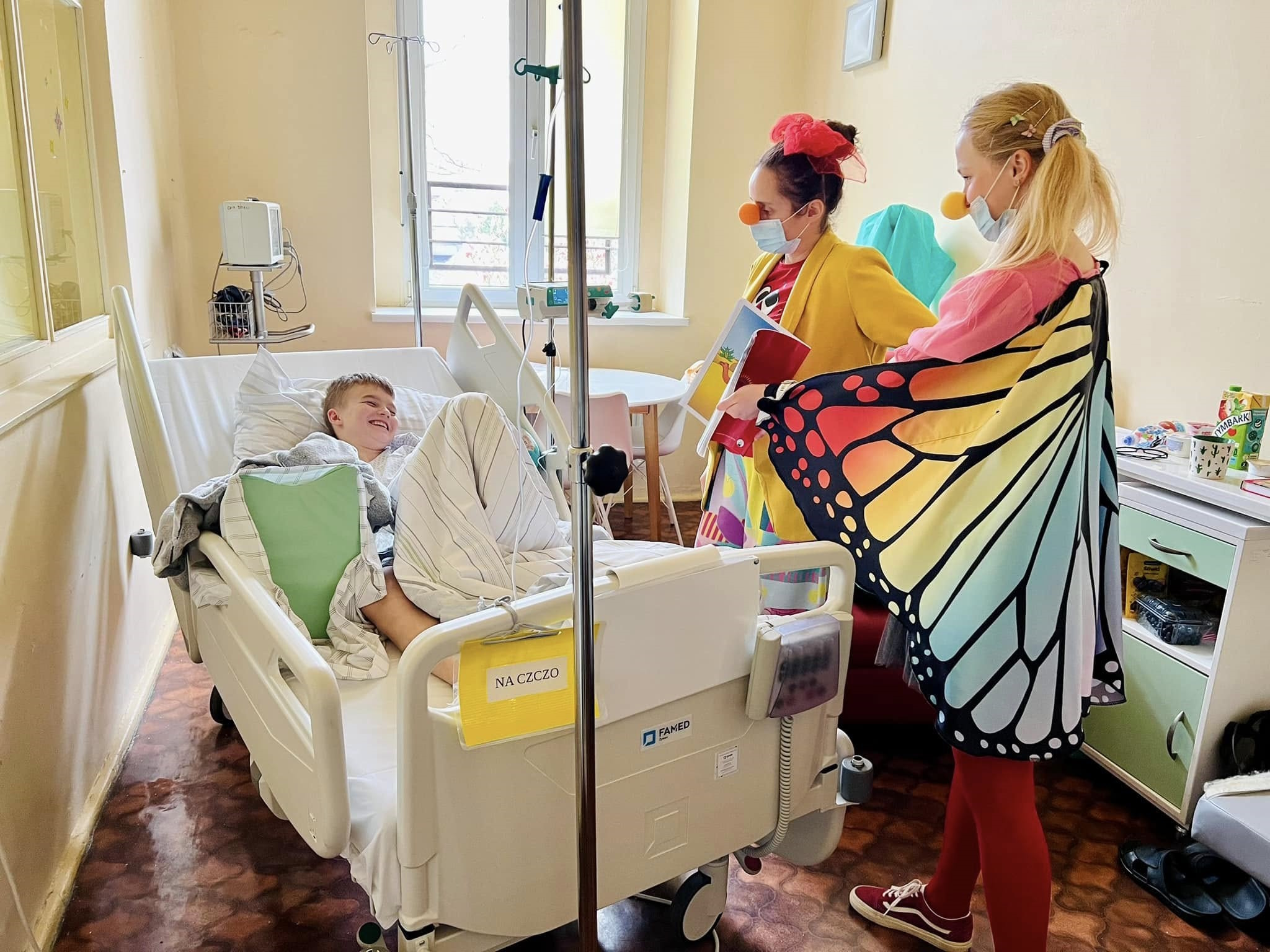 wolontariuszki ze skrzydłami motyla przy łóżku szpitalnym na którym leży chłopiec