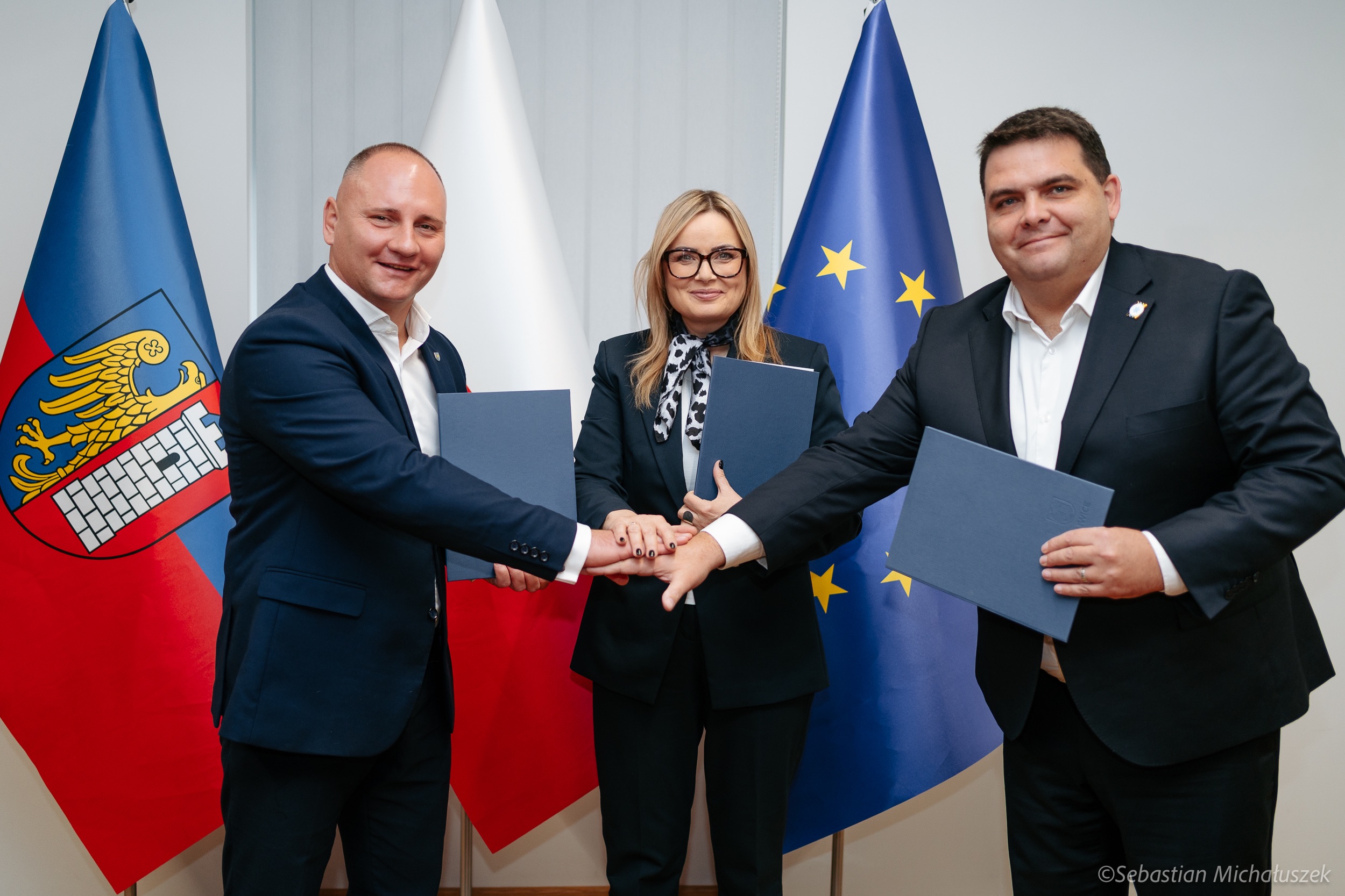 kobieta i dwóch mężczyzn z teczkami na tle flag