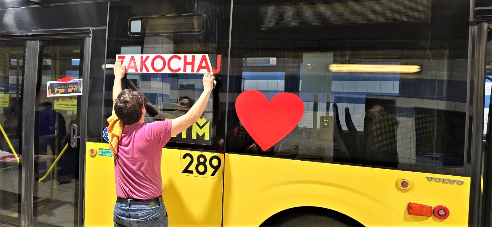 Mężczyzna nakleja walenktynkowe ozdoby na szyby żółtego autobusu