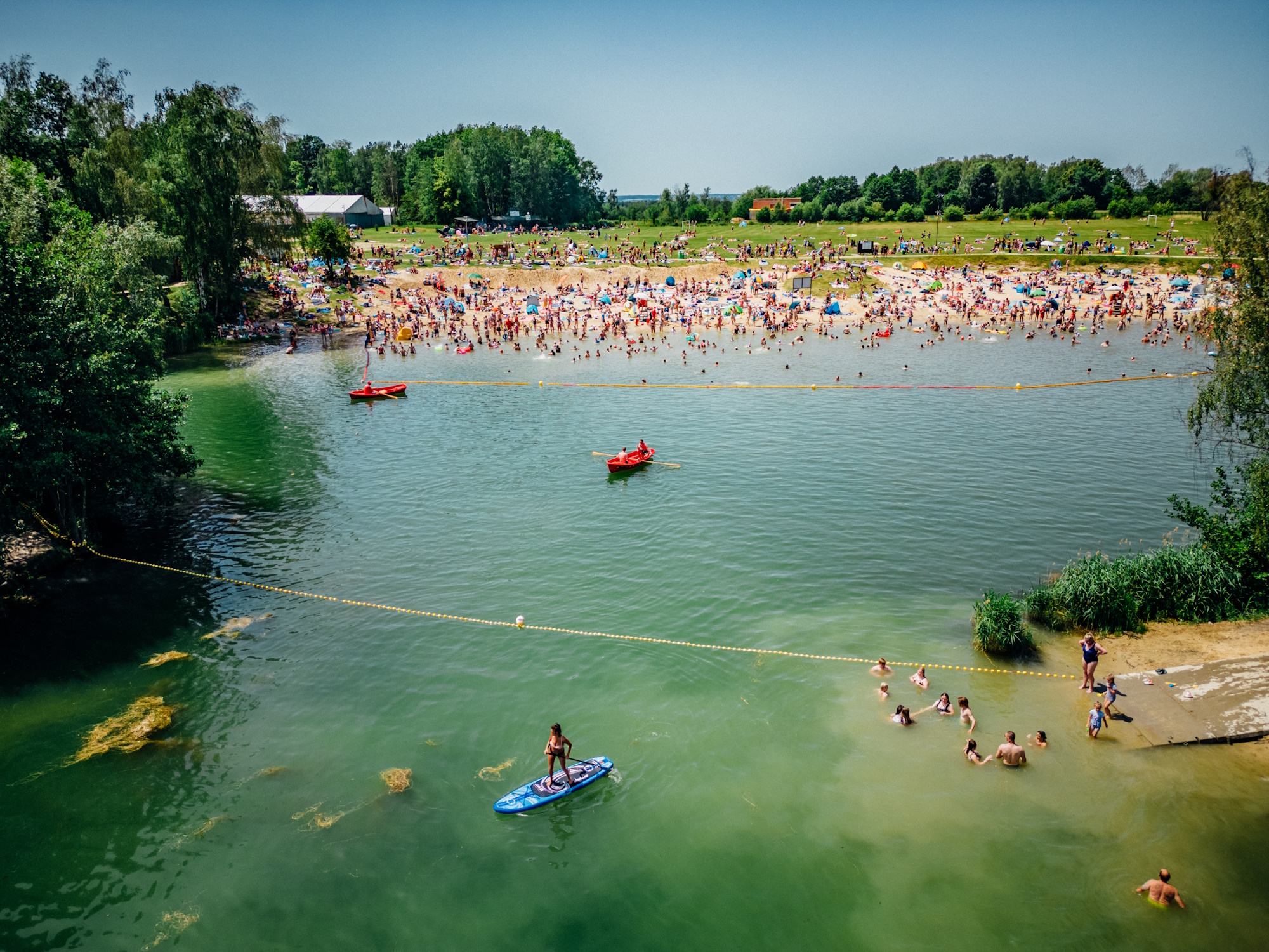 łódki na jeziorze, w tle ludzie na piaszczystej plaży