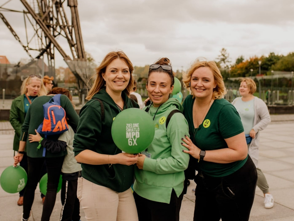 Trzy kobiety w zielonych bluzach. Jedna z nich trzyma zielony balonik z napisem: Zielone światło MPD. 6 października. W tle widać fragment wieży Radiostacji Gliwickiej.